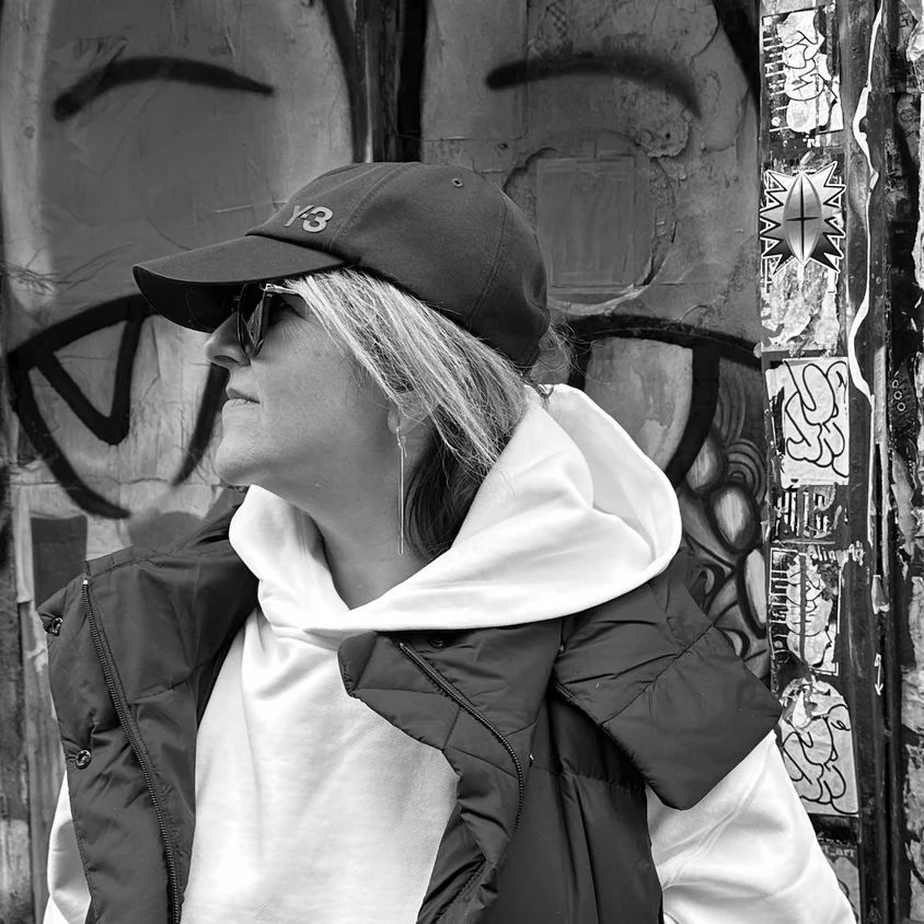Nicole Yershon in a cap, black and white portrait against a painted wall