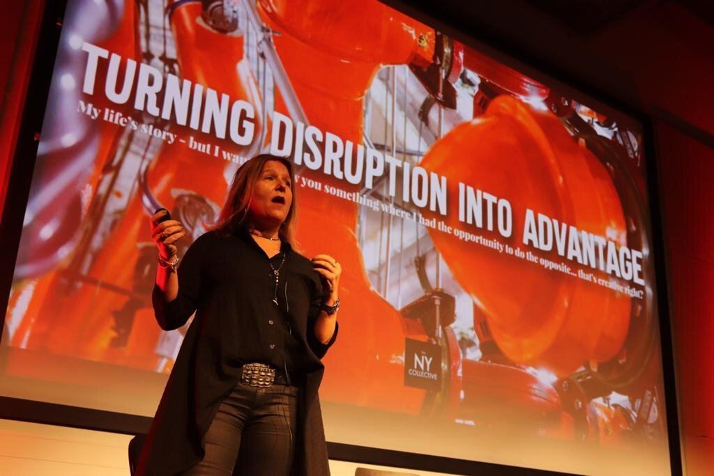 Nicole Yershon speaking on stage in front of a screen reading Turning Disruption Into Advantage